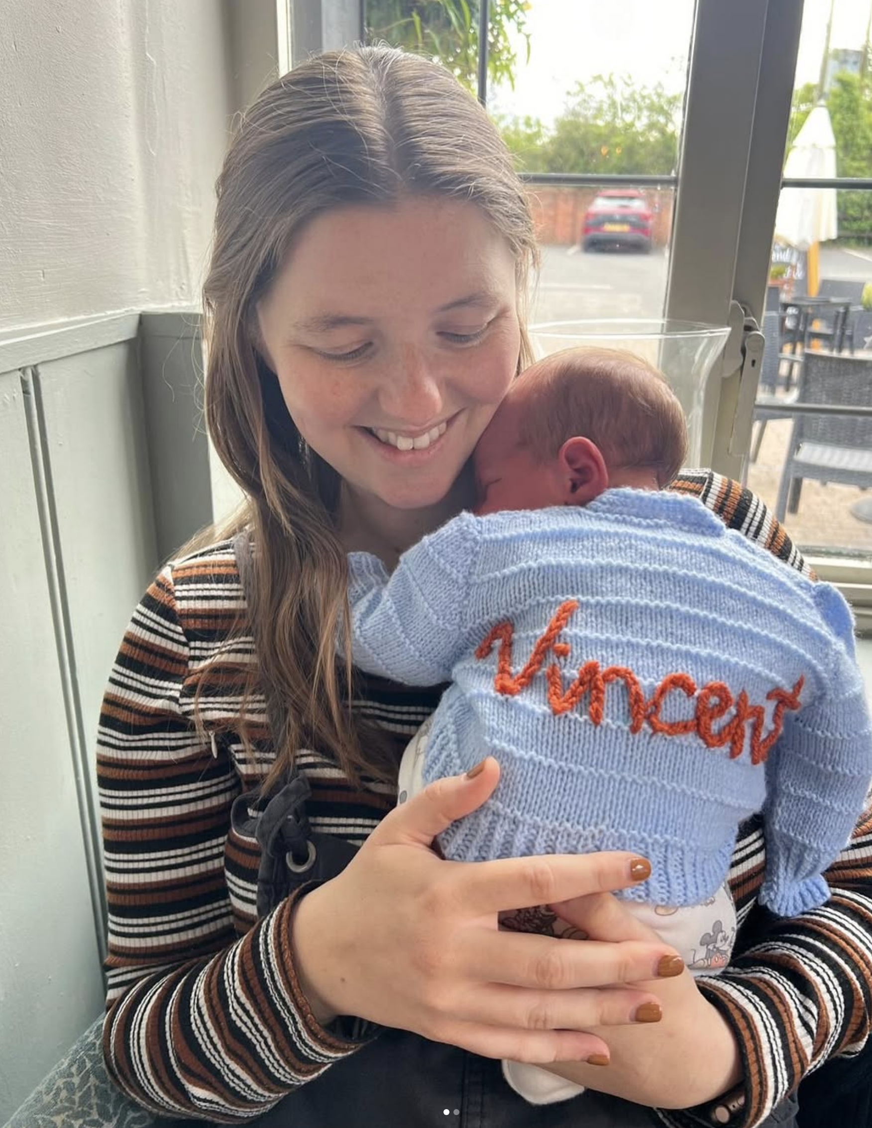 The maker holding a baby wearing a personalised knitted cardigan
