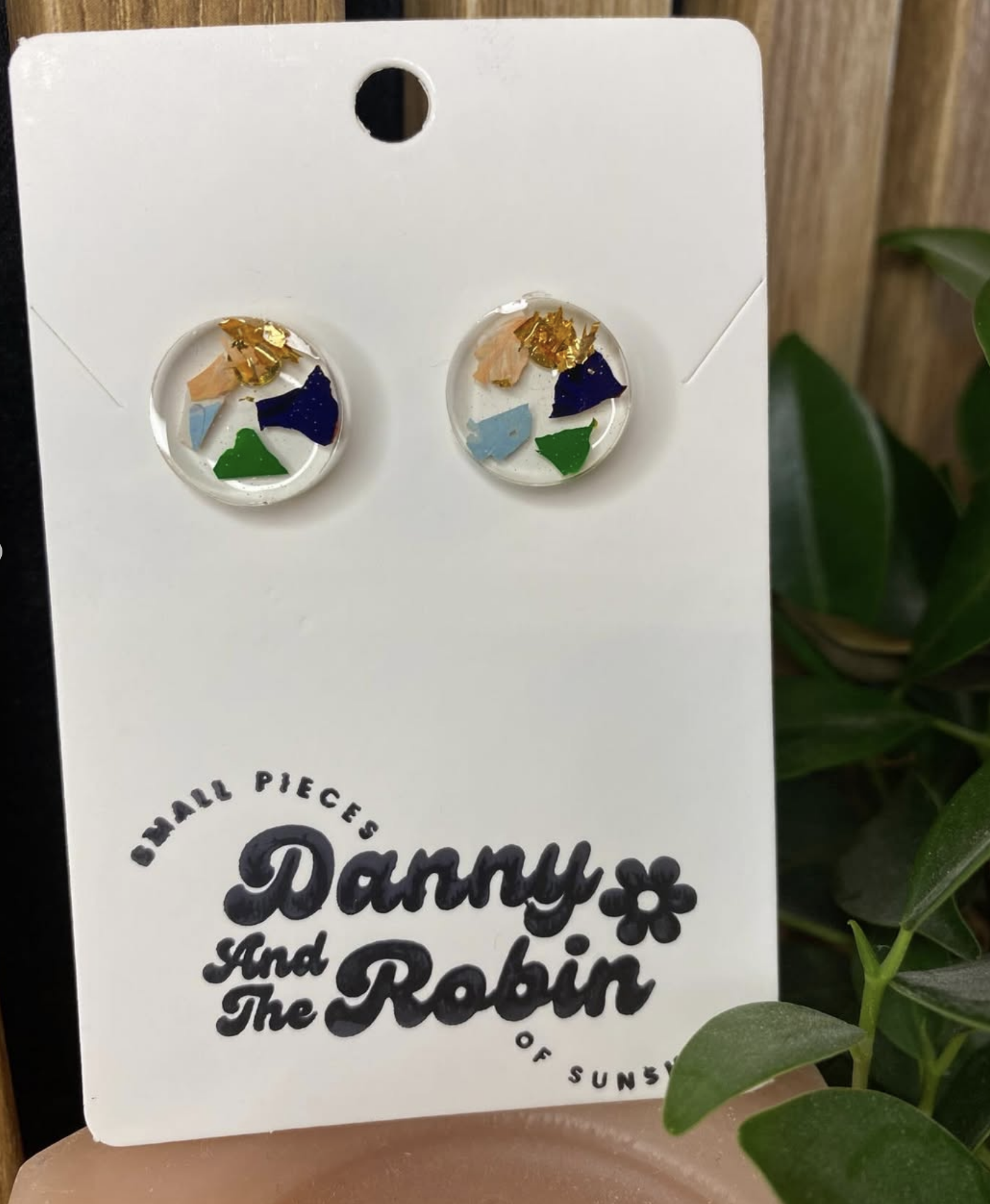 Handmade resin stud earrings with colourful geometric shapes inside a clear dome, on a branded jewellery card