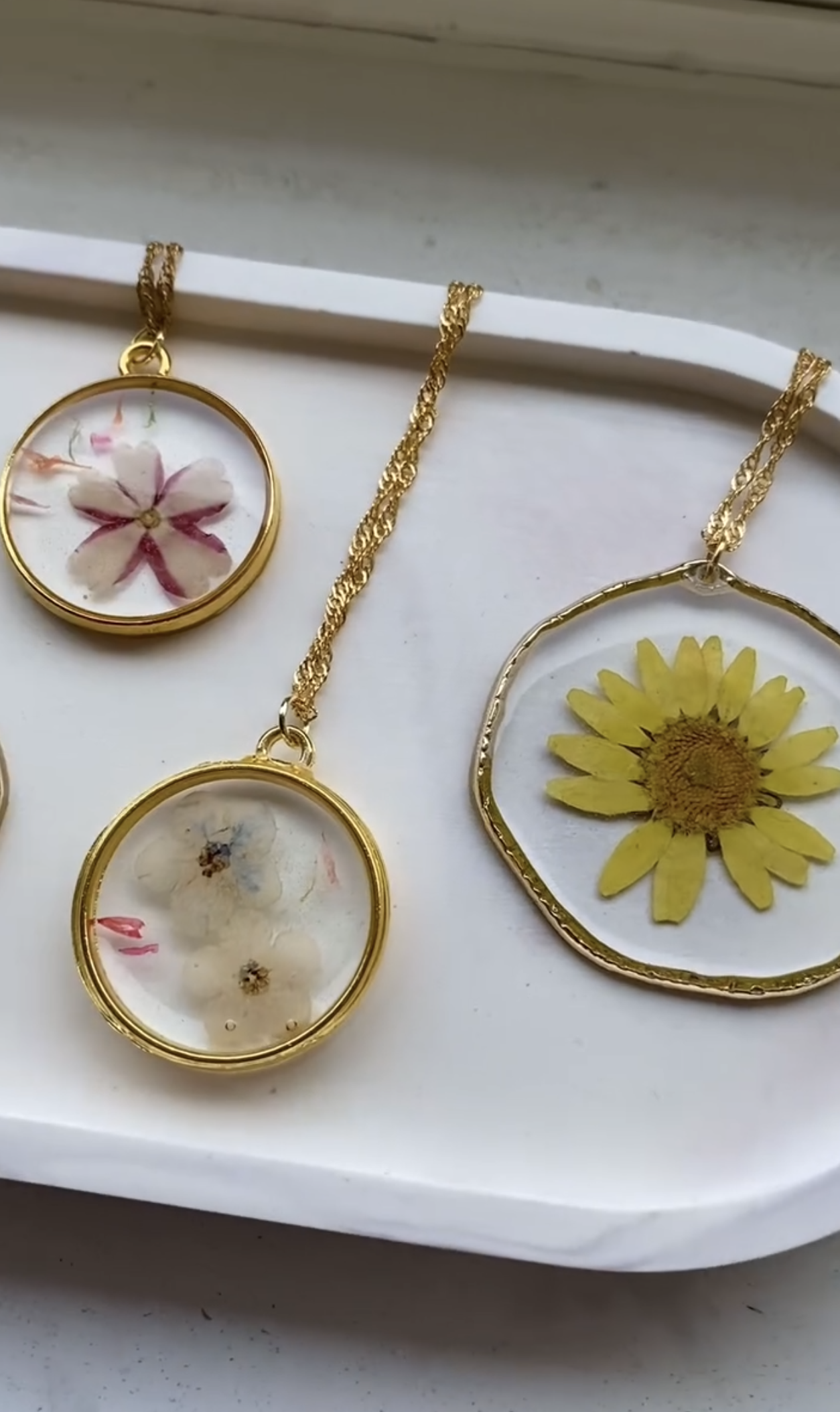 A collection of gold-framed pressed flower pendant necklaces, including floral and sunflower designs