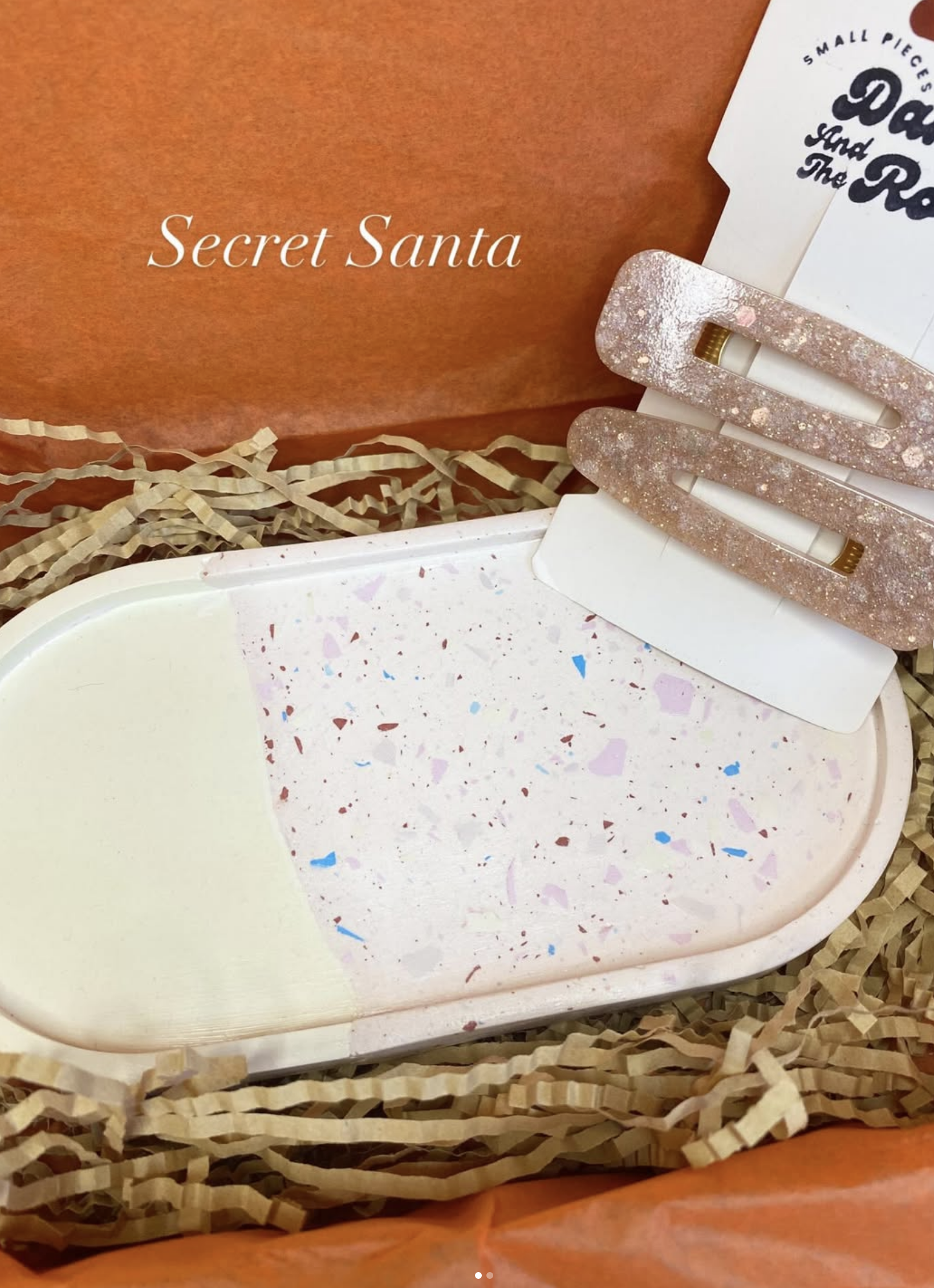 A terrazzo-patterned decorative tray and glittery hair clips presented in an orange Secret Santa gift box