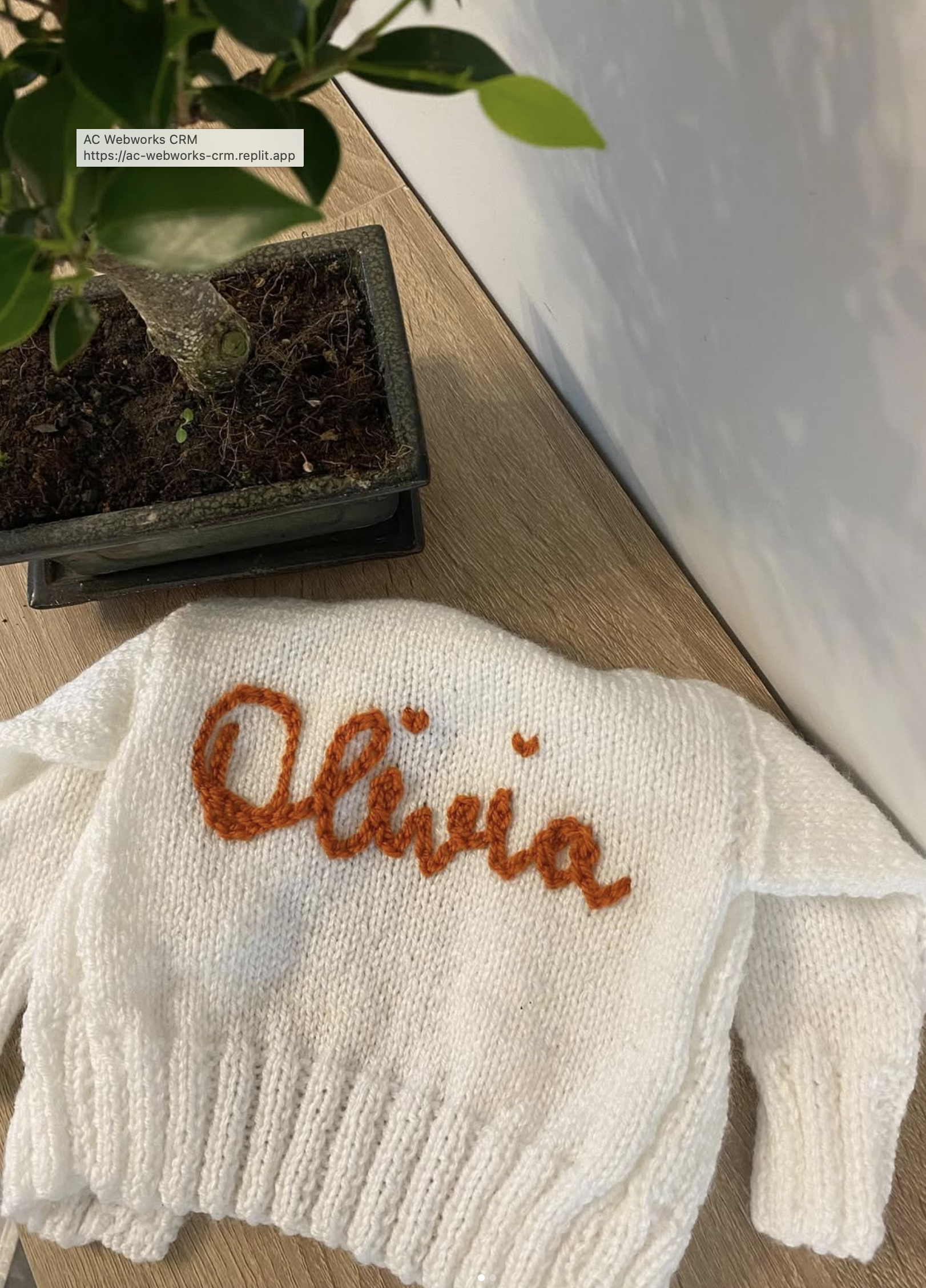 A white personalised hand-knitted baby cardigan with the name Olivia embroidered in orange lettering